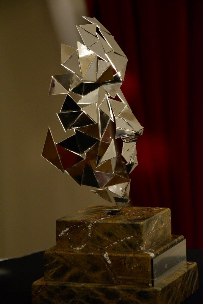 srebrna statuetka wykonana z kilkunastu błyszczących trójkątów, w całości przypomina pół twarzy, stoi na marmurowym postumencie