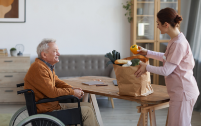 mężczyzna na wózku inwalidzkim patrzy na kobietę, która rozpakowuje torbę z zakupami, scena w pokoju 